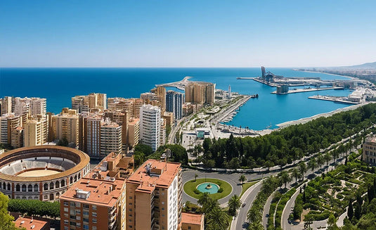 Vista panorámica de Málaga desde las alturas, con la Plaza de Toros de La Malagueta en primer plano, edificios residenciales, el puerto deportivo y el mar Mediterráneo extendiéndose hacia el horizonte bajo un cielo despejado.