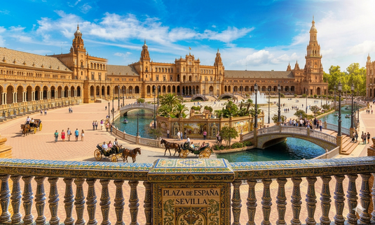 Vista panorámica de la Plaza de España en Sevilla, con su arquitectura semicircular, canales, puentes y detalles de azulejos típicos andaluces.