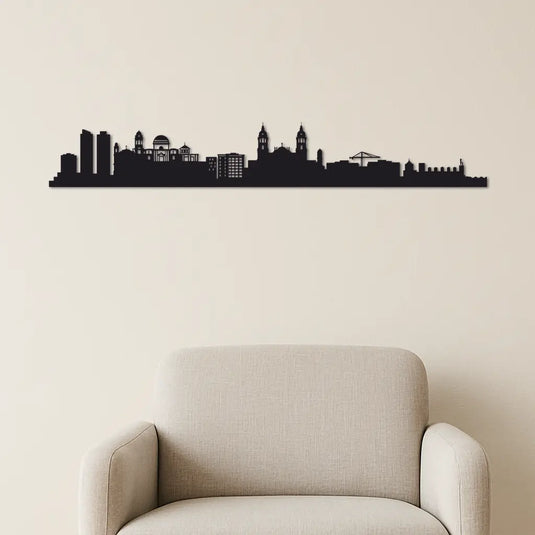 Skyline decorativo de la ciudad de Cádiz en madera DM sobre sofá moderno beige. Decoración de pared minimalista con silueta negra artesanal, ideal para salones con estilo contemporáneo. Producto hecho a mano inspirado en el perfil urbano de Cádiz.